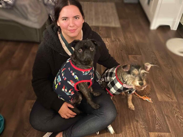 Kasey, Pet Care Provider, sitting cross-legged, holding her two small dogs.